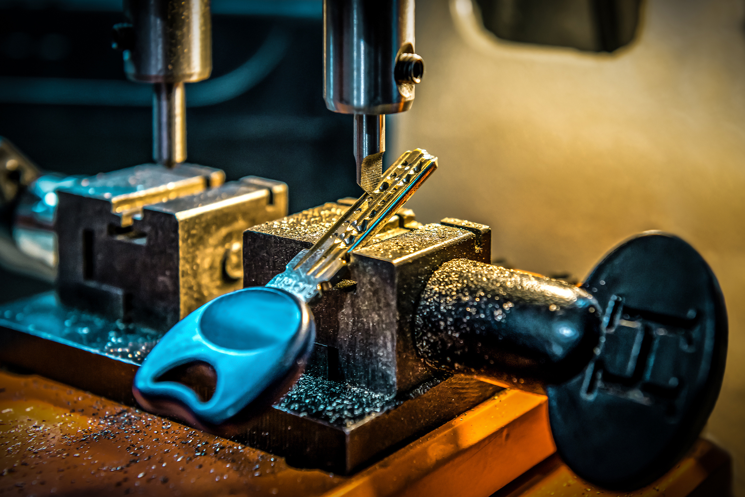 A close-up view of a key being cut by a machine, with metal shavings scattered around. The key is securely held in place as the cutting tool shapes its grooves.