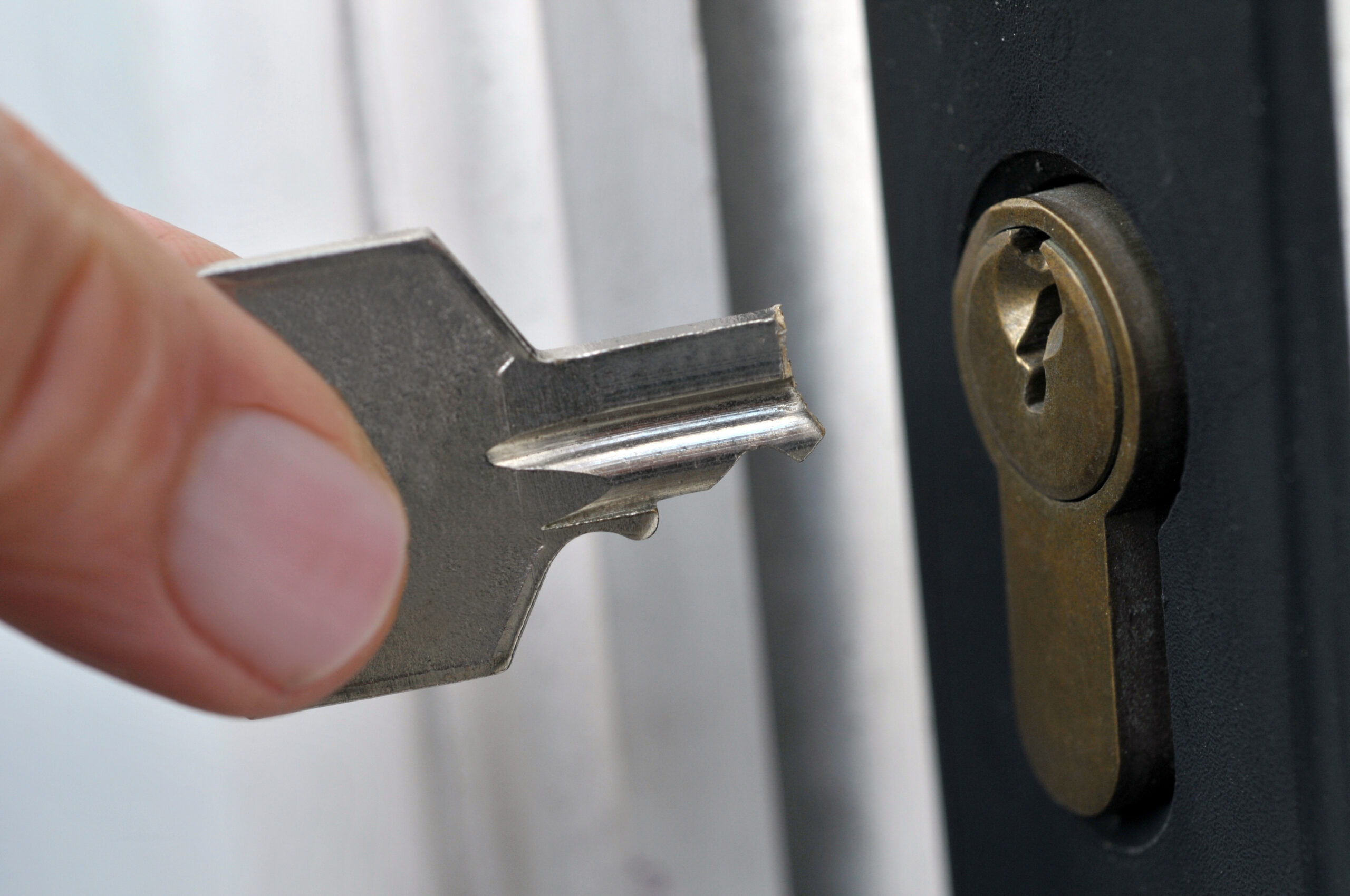 A close-up of a hand holding a broken key near a door lock, with the jagged edge of the key visible, about to insert it into the keyhole.